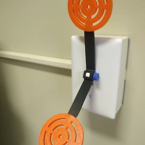 May include: A white light switch with a black lever attached to two orange circular targets. The targets have concentric circles and a small hole in the center.