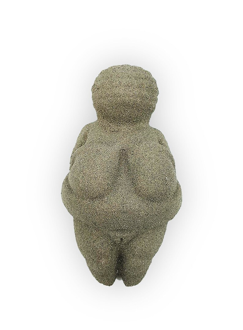 Puede incluir: Una peque&ntilde;a escultura de piedra gris que representa una figura femenina con rasgos exagerados. La escultura es lisa y tiene una superficie ligeramente texturizada.