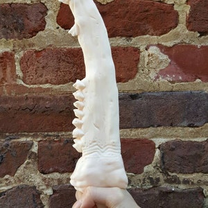 May include: A white, detailed, 3D printed dagger with a serrated edge and a textured handle.
