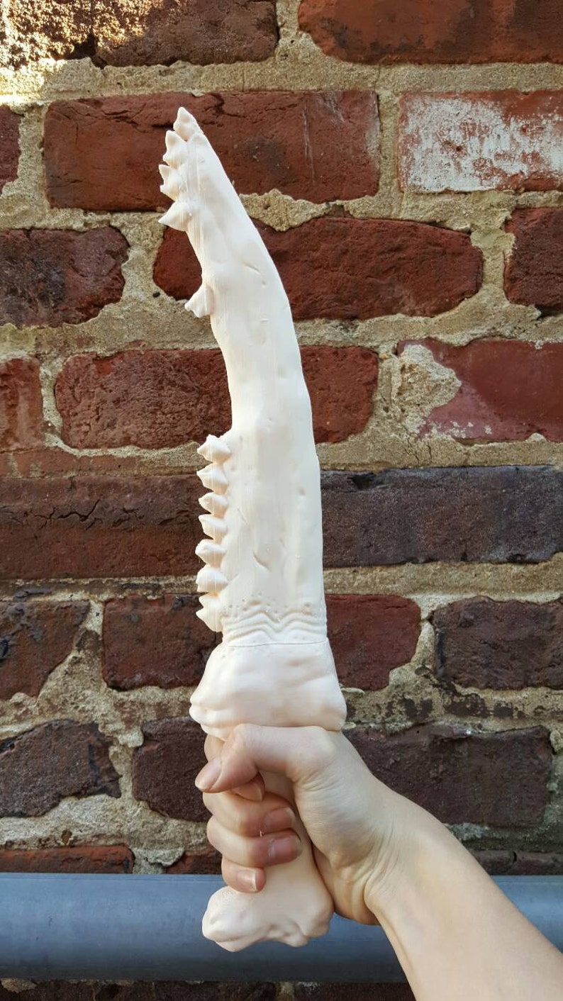 May include: A white, detailed, 3D printed dagger with a serrated edge and a textured handle.