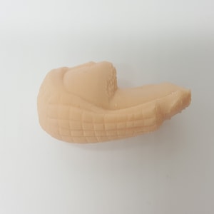 May include: A close-up of a beige, textured, 3D printed object. The object is shaped like a curved, elongated shape with a slightly pointed end.