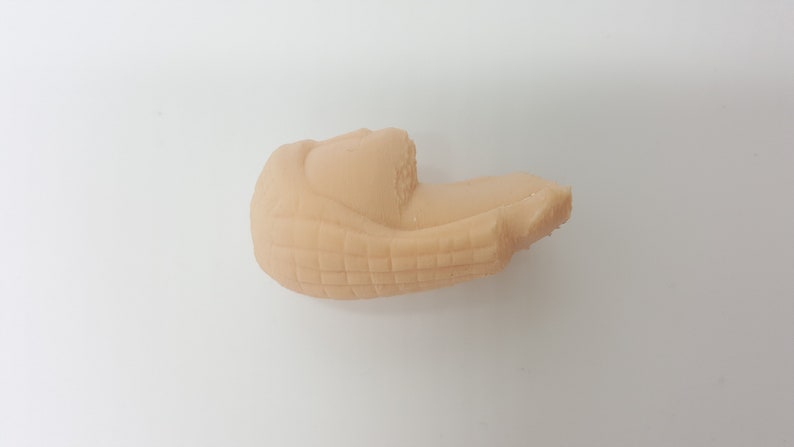 May include: A close-up of a beige, textured, 3D printed object. The object is shaped like a curved, elongated shape with a slightly pointed end.