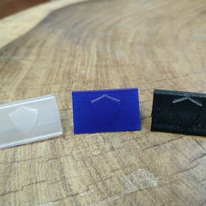 May include: Three small plastic shields, one clear, one blue, and one black. Each shield has a raised design of a shield.