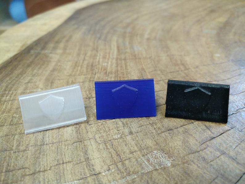 May include: Three small plastic shields, one clear, one blue, and one black. Each shield has a raised design of a shield.