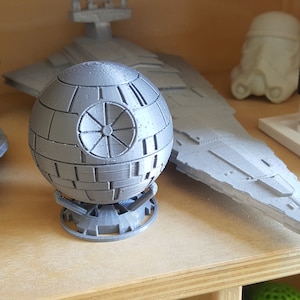 May include: A collection of gray 3D printed Star Wars models, including a Death Star, a TIE fighter, and a Star Destroyer. The models are displayed on a wooden shelf.