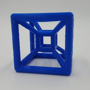 Puede incluir: Un cubo azul impreso en 3D con un centro hueco y un cubo m&aacute;s peque&ntilde;o en su interior.