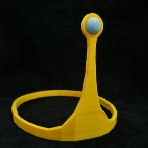 May include: A yellow plastic crown with a blue jewel on top. The crown is designed to fit on a person's head.