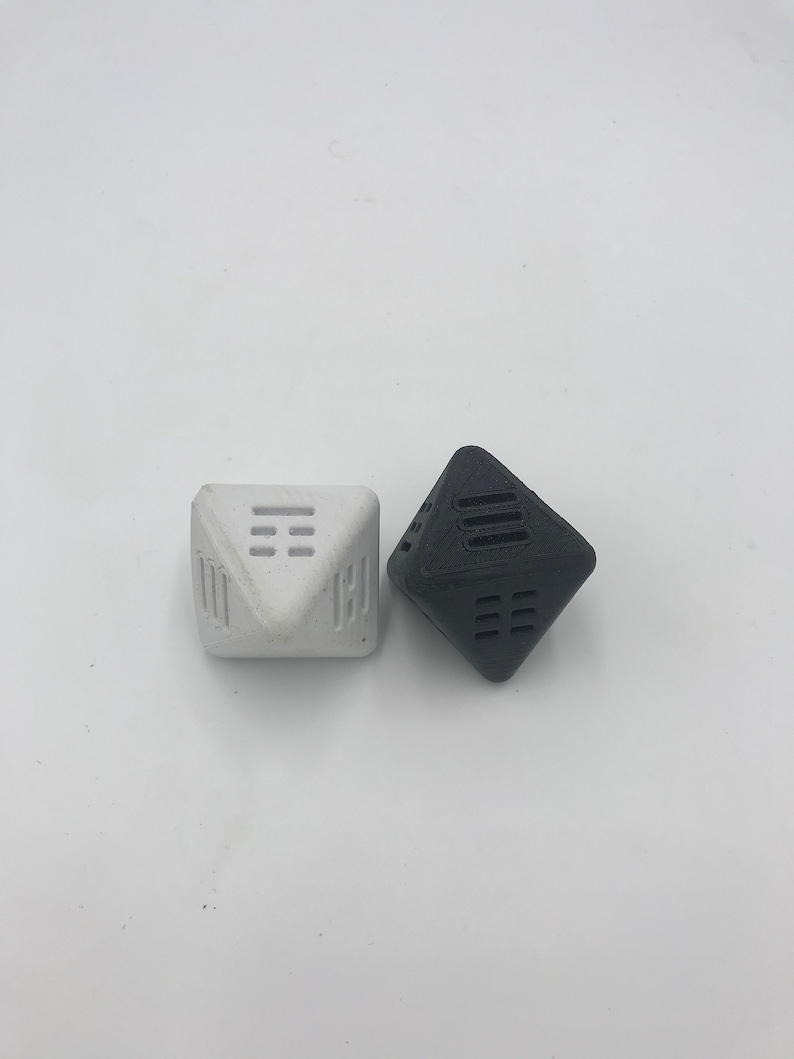 May include: Two geometric dice, one white and one black, with a unique design of lines and squares on each face.