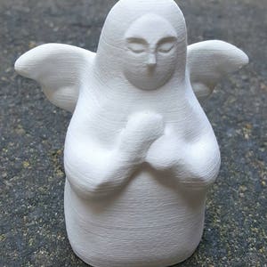 May include: White ceramic figurine of an angel with wings, closed eyes, and hands clasped in prayer.
