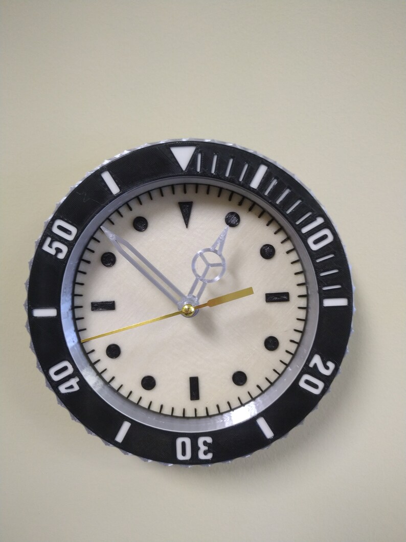 Puede incluir: Un reloj anal&oacute;gico blanco y negro con una esfera blanca y agujas negras. El reloj tiene un bisel negro con n&uacute;meros blancos alrededor del borde. Los n&uacute;meros son 10, 20, 30, 40 y 50.