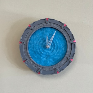 May include: A grey and red clock shaped like the Stargate from the TV show Stargate SG-1. The clock face is a blue swirling pattern.