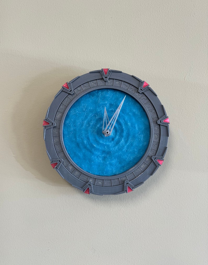 May include: A grey and red clock shaped like the Stargate from the TV show Stargate SG-1. The clock face is a blue swirling pattern.