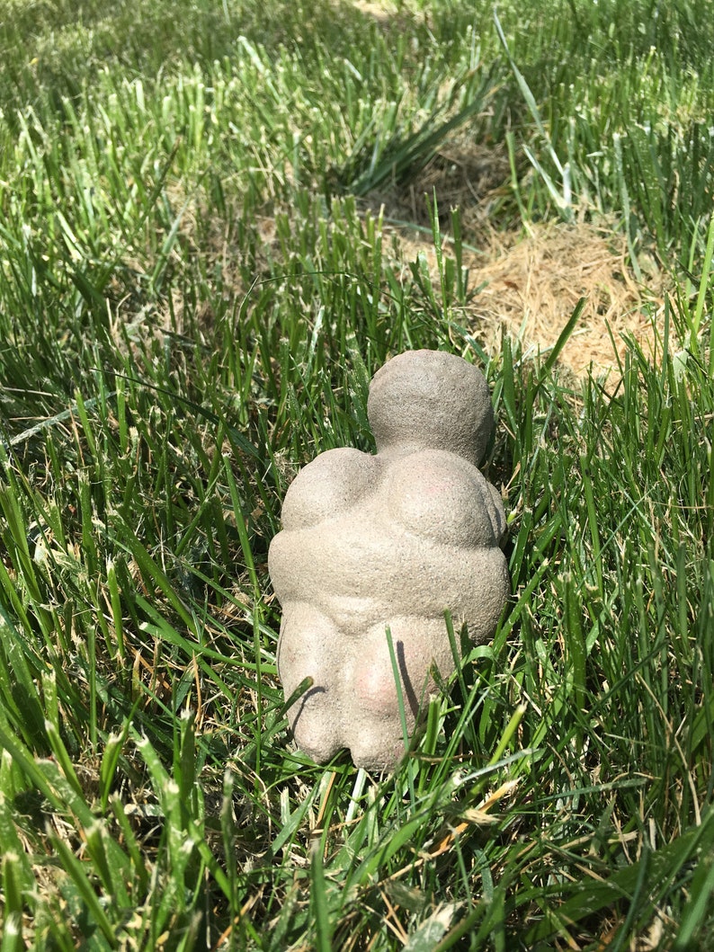Puede incluir: Una escultura de piedra gris de una persona sentada. La escultura est&aacute; en un &aacute;rea cubierta de hierba.