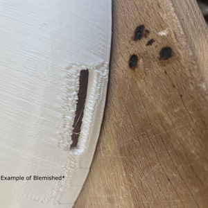 May include: Close-up of a white 3D printed object with a visible imperfection or blemish. The object is resting on a wooden surface.