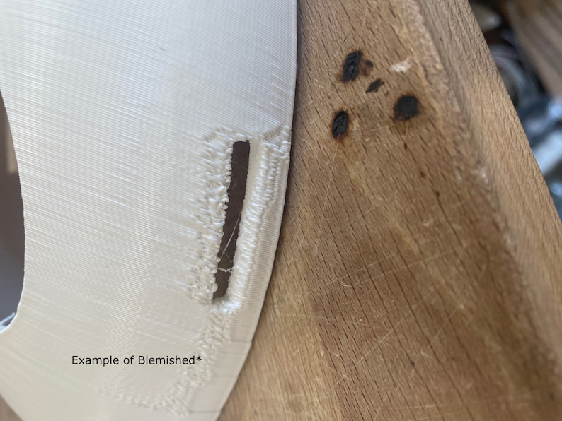 May include: Close-up of a white 3D printed object with a visible imperfection or blemish. The object is resting on a wooden surface.