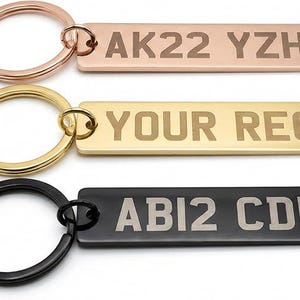 May include: Three personalised keyrings in rose gold, gold, and black. Each rectangular tag has engraved text: "AK22 YZH", "YOUR REG", and "ABI2 CDE". The keyrings are attached to the tags.