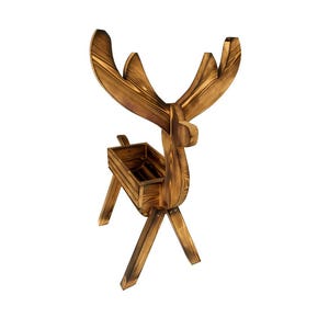 May include: A wooden reindeer planter with a rustic, burnt-wood finish. The planter has a rectangular box for plants and large antlers. The reindeer stands on four angled legs, creating a decorative and functional piece.