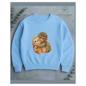 May include: A light blue sweatshirt featuring an embroidered design of two hugging monkeys. The monkeys are brown and tan, with detailed facial features. The text "White Bear" is in the upper right corner.