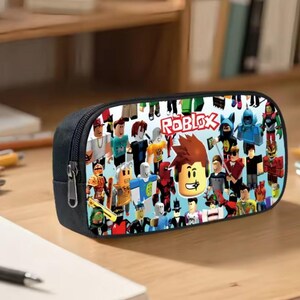 Puede incluir: Estuche negro con un dise&ntilde;o colorido que presenta varios personajes de Roblox y el logotipo de Roblox. El estuche tiene un cierre de cremallera y probablemente est&aacute; hecho de una tela resistente.