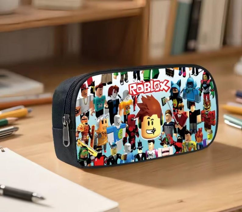 Puede incluir: Estuche negro con un dise&ntilde;o colorido que presenta varios personajes de Roblox y el logotipo de Roblox. El estuche tiene un cierre de cremallera y probablemente est&aacute; hecho de una tela resistente.