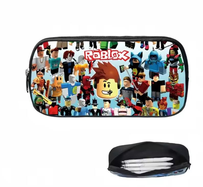 Puede incluir: Estuche negro con un dise&ntilde;o colorido con varios personajes de Roblox y el logotipo de Roblox. El estuche tiene cierre de cremallera e interior negro. Debajo se ve un segundo estuche abierto con bol&iacute;grafos.