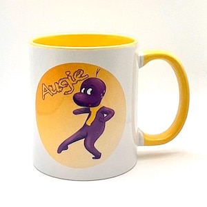 May include: White ceramic mug with a yellow interior and handle. The mug features a cartoon character named Augie in purple and yellow on a yellow and orange background.