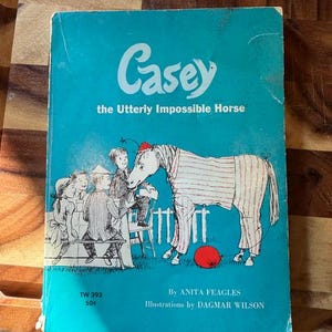 Könnte beinhalten: Ein Vintage-Kinderbuch mit dem Titel "Casey the Utterly Impossible Horse". Das türkisfarbene Cover zeigt Illustrationen von Kindern und einem Pferd in gestreiften Pyjamas. Das Buch stammt von Anita Feagles, mit Illustrationen von Dagmar Wilson.