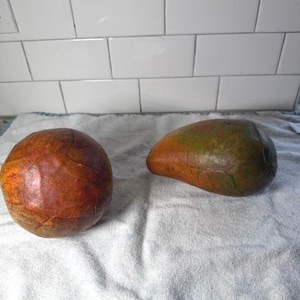 May include: Two decorative objects with a textured, crackled finish. One object is a spherical, reddish-brown item, while the other is an elongated, pear-shaped piece featuring a blend of green, brown, and yellow tones with a visible crackled surface.