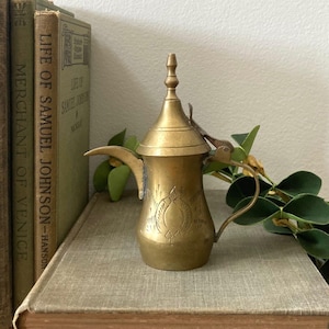 May include: A white ceramic mug with a black handle and the text "But First, Coffee" in a black, bold font. The mug is on a white surface.