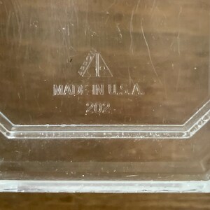 K&ouml;nnte beinhalten: Klarer, achteckiger Glasbeh&auml;lter mit der Aufschrift "MADE IN U.S.A." und der eingravierten Nummer "202". Der Beh&auml;lter hat ein geometrisches Design, m&ouml;glicherweise Vintage.