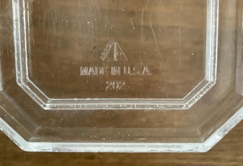 K&ouml;nnte beinhalten: Klarer, achteckiger Glasbeh&auml;lter mit der Aufschrift "MADE IN U.S.A." und der eingravierten Nummer "202". Der Beh&auml;lter hat ein geometrisches Design, m&ouml;glicherweise Vintage.
