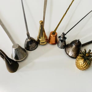 May include: An assortment of vintage metal bottle stoppers in various shapes and colors. The stoppers include a gold pineapple, a copper bell, and a silver cone. Each stopper has a long, thin handle.