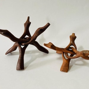 May include: Two wooden display stands. The larger stand is dark brown and has a starburst design. The smaller stand is light brown and has a similar design. Both stands are made of carved wood.