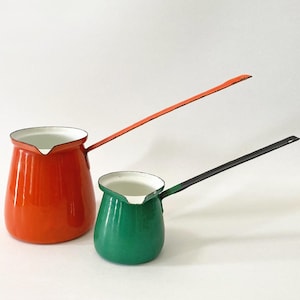May include: Two vintage enamelware coffee pots. One is a vibrant orange with a matching handle, the other is a deep green with a black handle. Both have white interiors and are set against a white background.