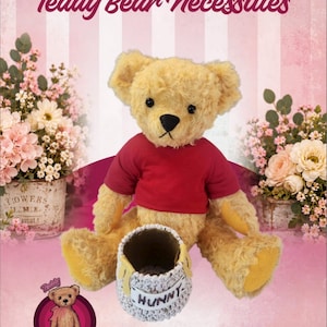 Könnte beinhalten: Ein 18 Zoll großer Sunny Teddybär mit goldbraunem Fell trägt ein schlichtes rotes T-Shirt. Der Bär sitzt hinter einem kleinen, strukturierten, hellen Häkeltopf, auf dessen Vorderseite das Wort HUNNY mit dunklem Garn gestickt ist.