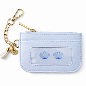 May include: A light blue cardholder with a gold zipper, chain, and clasp. The cardholder has a clear window with two blue seashell designs. A white tassel and gold charm hang from the chain.