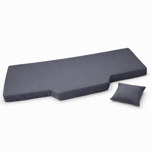 Op de afbeelding: Een donkergrijze, rechthoekige matras met een uitgesneden gedeelte en een klein vierkant kussen. De matras is gemaakt van een zacht, gewatteerd materiaal. Het kussen heeft dezelfde kleur als de matras.