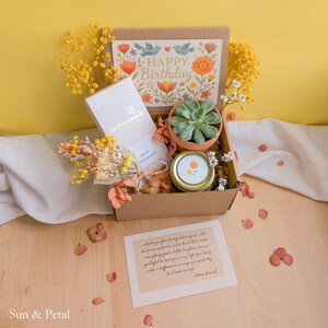 May include: A cardboard gift box containing a Moonstruck milk chocolate bar, a small succulent in a terracotta pot, a jar with a gold lid, and dried yellow flowers. The box lid features a floral Happy Birthday print and a handwritten note.