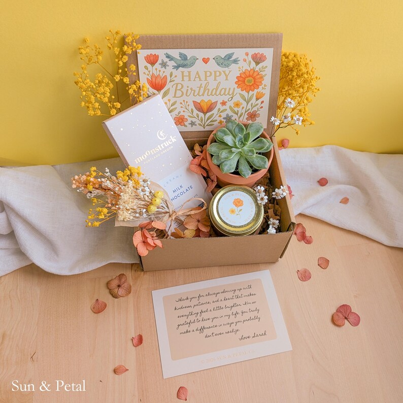 May include: A cardboard gift box containing a Moonstruck milk chocolate bar, a small succulent in a terracotta pot, a jar with a gold lid, and dried yellow flowers. The box lid features a floral Happy Birthday print and a handwritten note.