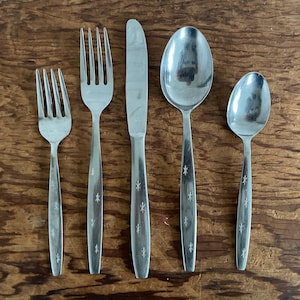 May include: A five-piece stainless steel flatware set consisting of a small fork, a large fork, a dinner knife, a large spoon, and a small spoon. Each handle features a polished silver finish with a repeating etched starburst pattern.