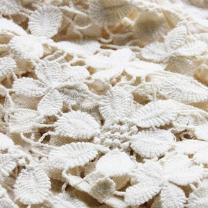 May include: Close-up of a white crocheted fabric with a delicate floral pattern.