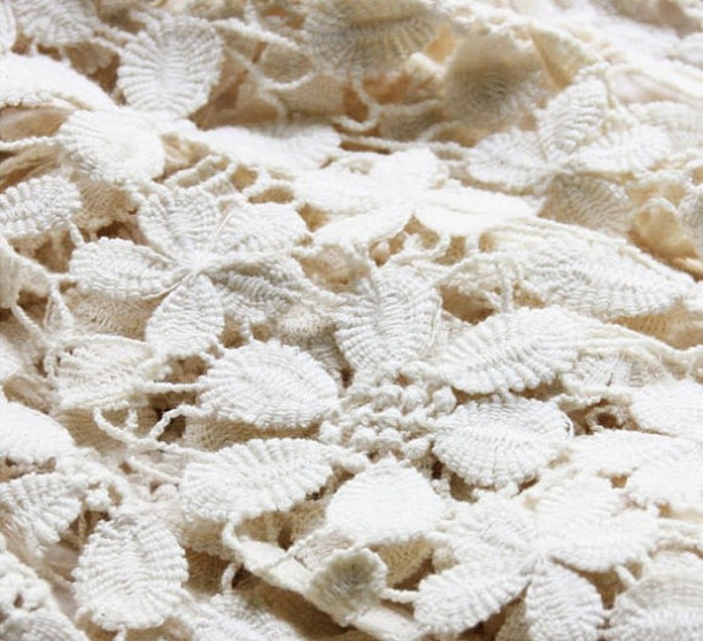May include: Close-up of a white crocheted fabric with a delicate floral pattern.