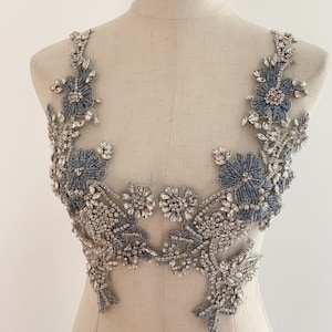 Puede incluir: Una delicada aplicación de cuentas plateadas y azules con diseños florales y adornos de cristal. Esta aplicación es perfecta para añadir un toque de brillo y elegancia a la ropa o los accesorios.