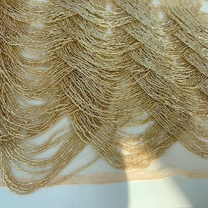 Puede incluir: Borde de cuentas doradas con un diseño delicado y fluido. El borde está hecho de pequeñas cuentas redondas que están enhebradas juntas en un patrón de ondas en cascada. Las cuentas son de color dorado claro y tienen un brillo sutil.