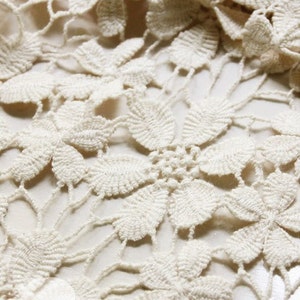 May include: Close-up of a white crocheted fabric with a delicate floral pattern.