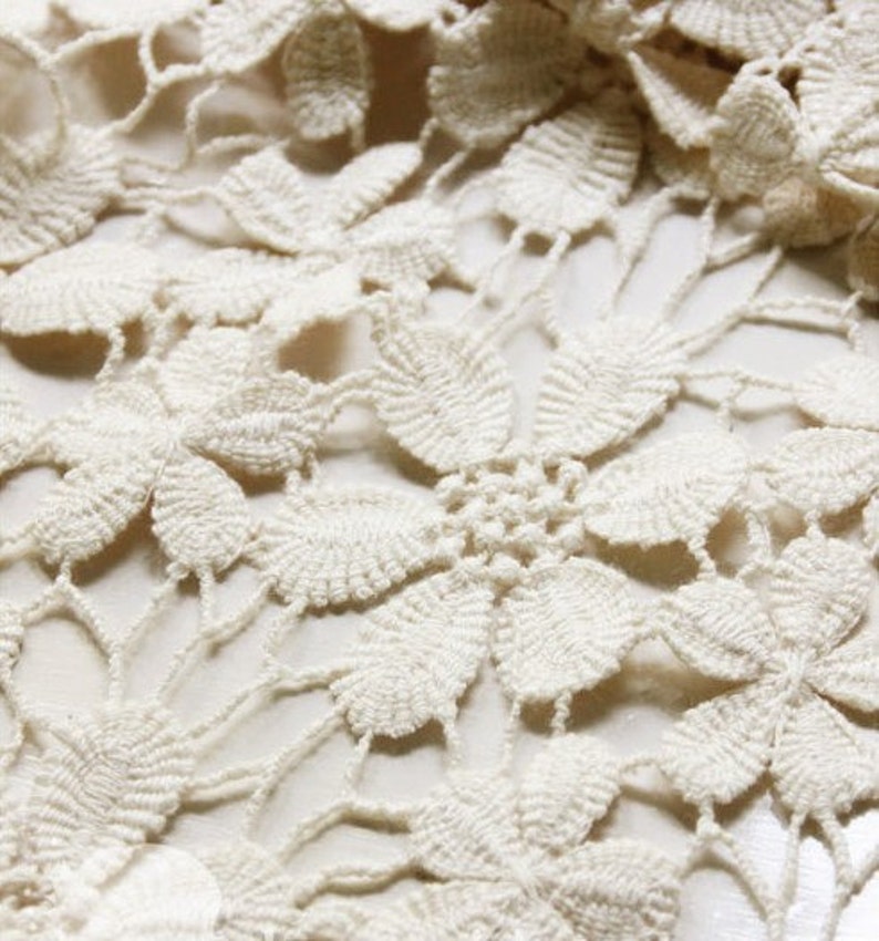 May include: Close-up of a white crocheted fabric with a delicate floral pattern.