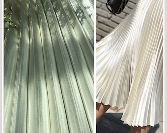 May include: A white pleated skirt with a satin-like sheen. The skirt is made of a lightweight fabric and has a flowing silhouette.