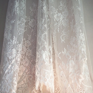 May include: White lace fabric with a delicate floral pattern. The fabric is sheer and has a soft, flowing texture.