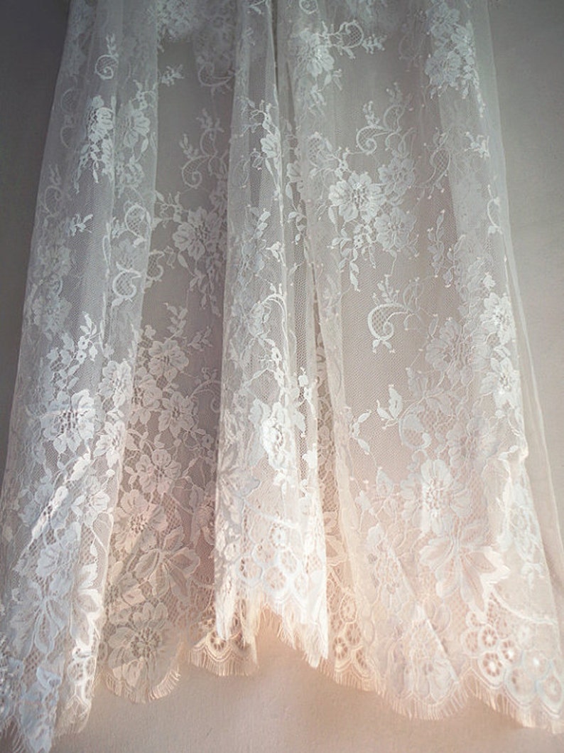 May include: White lace fabric with a delicate floral pattern. The fabric is sheer and has a soft, flowing texture.
