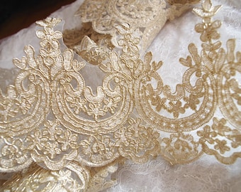 May include: Gold lace trim with a delicate floral pattern. The lace is on a white background.